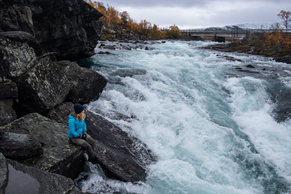 girl sitting next to waterfall in the mountains of Norway