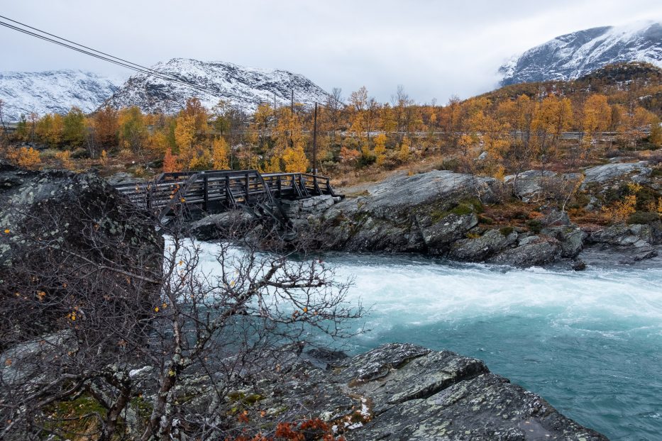 snowy mountains and blue water in a river with autumn colors around