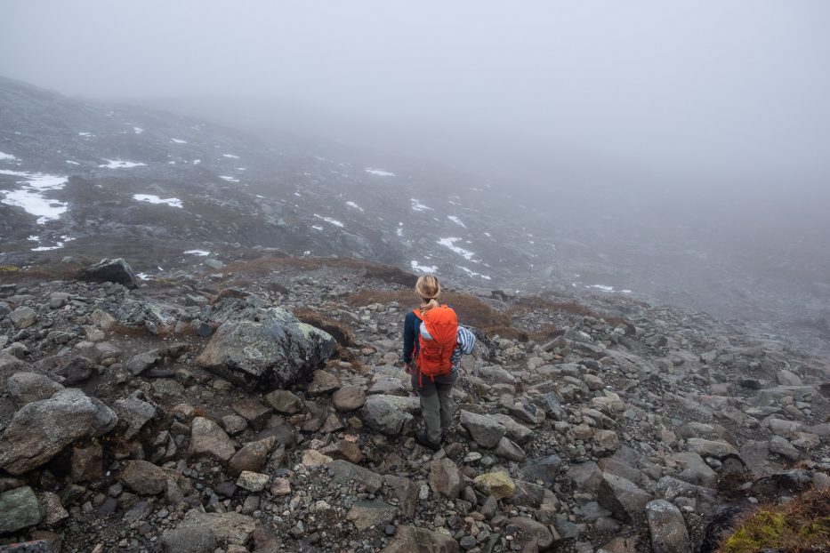 person with orange backpack in a foggy mountain landscape