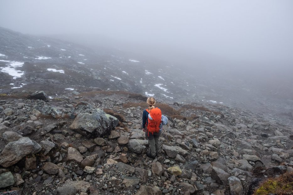 person med oransje sekk står i fjellet med mye tåke