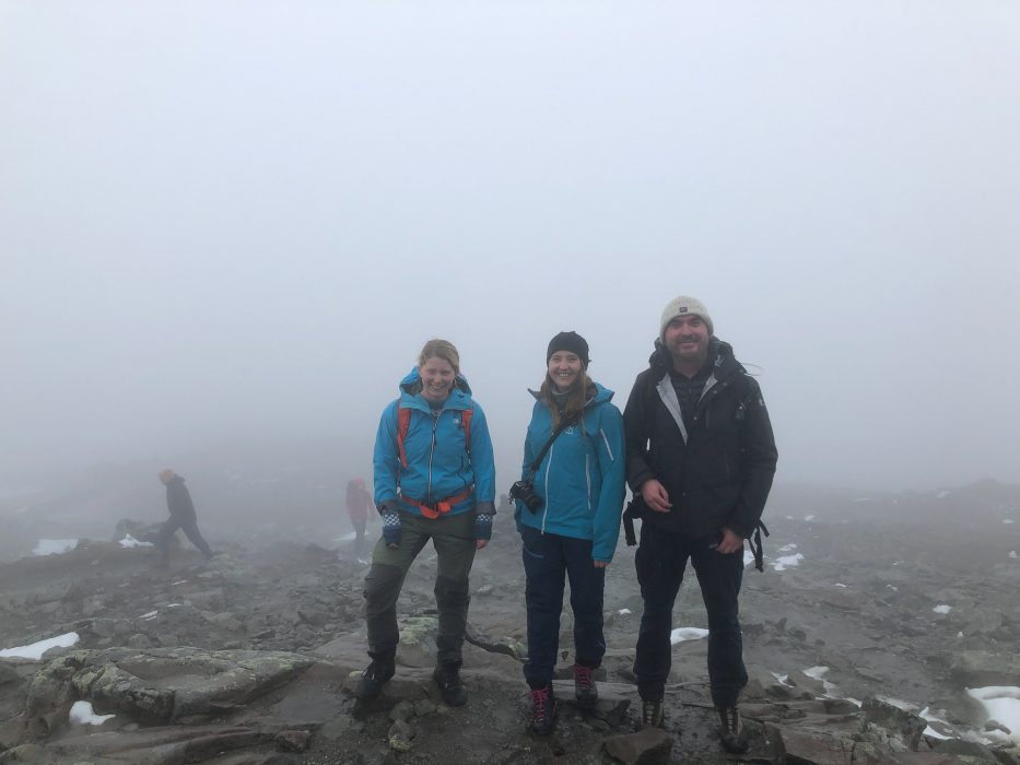 three people standing on top of bitihorn with the only view being fog
