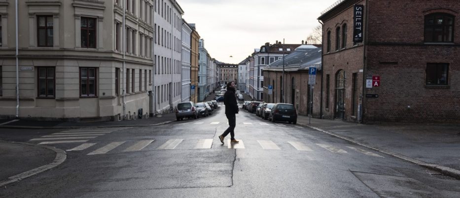 Lone man crossing a road with colourful houses in Oslo Norway