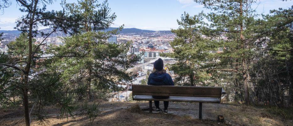 Jente sitter på benk i skogen og ser utover Oslo by nedenfor seg
