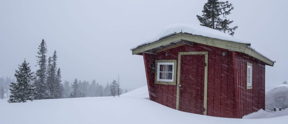 En liten rød hytte i skogen med masse snø