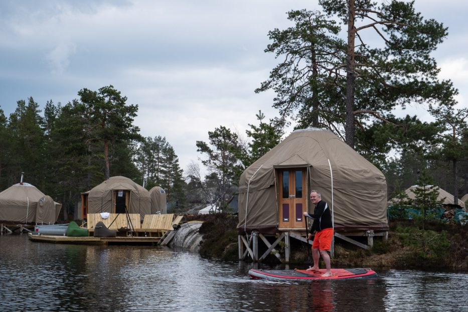 man standing on a sup in front of yurts at canvas telemark
