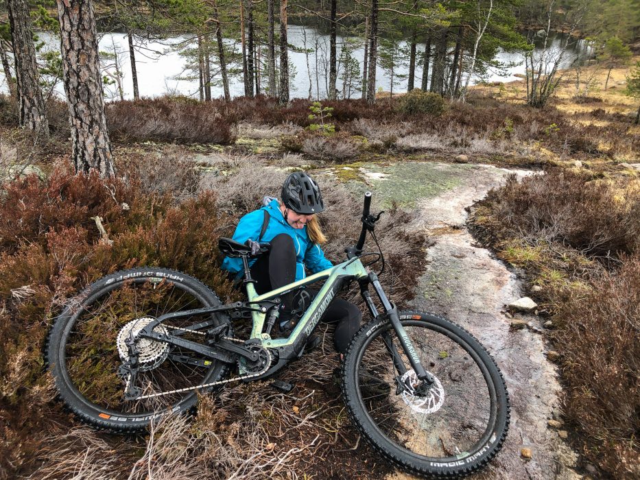 woman underneath a trail bike in a forest