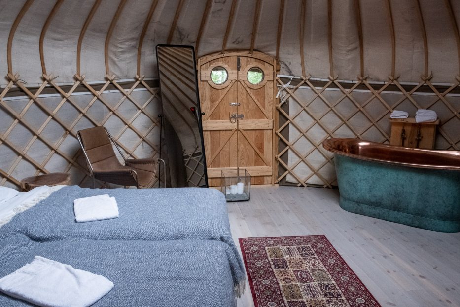 The inside of a luxury yurt at canvas hove with a huge bed, chair, mirror, door, bath tub and carpet