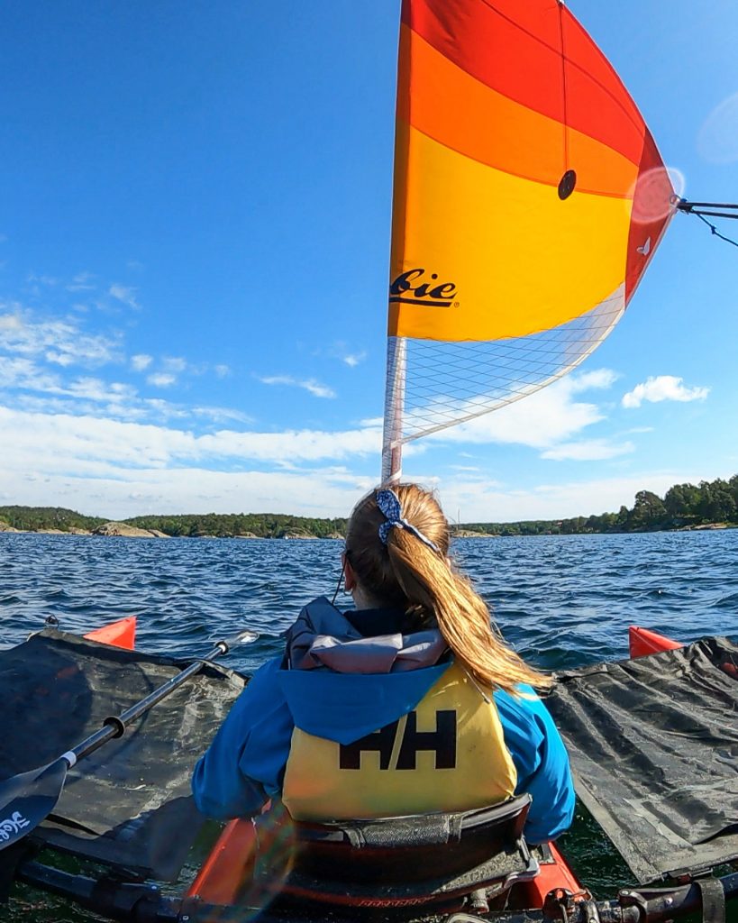 kvinne sitter i en trimaran med mangefarget seil