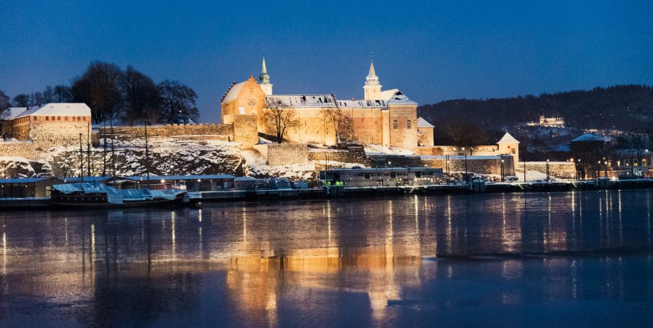 Akershus Fortress lit up at night with reflections in the water