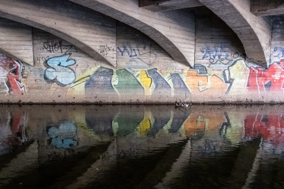 Grafitti på bru med refleksjoner i vannet langs Akerselva