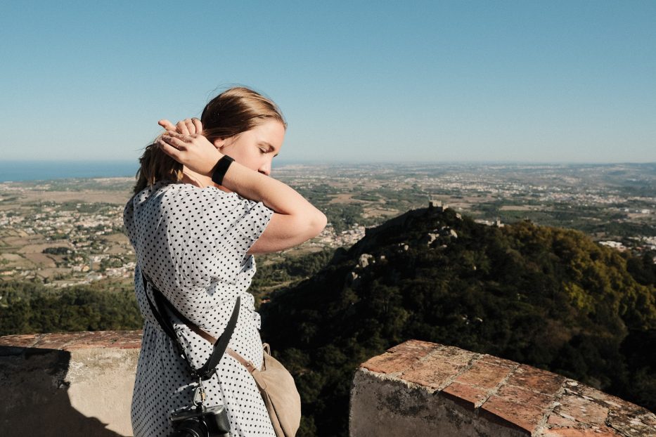 Jente i prikkete kjole retter på håret ved et utsiktspunkt i Sintra