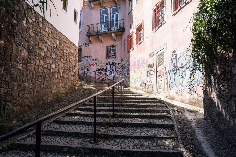 cobblestone road with a pink building filled with graffiti in the back