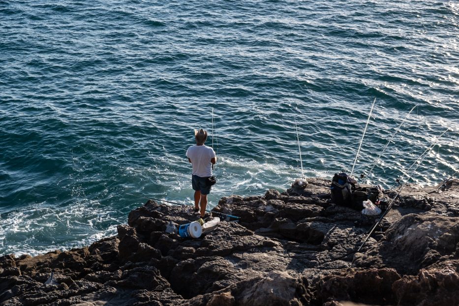 en fisker står og ser utover havet med flere fiskestenger oppstilt ved siden av seg