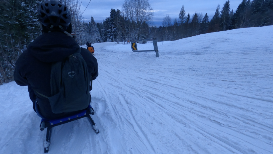 the back of a man sitting on a sledge driving down a hill with snow