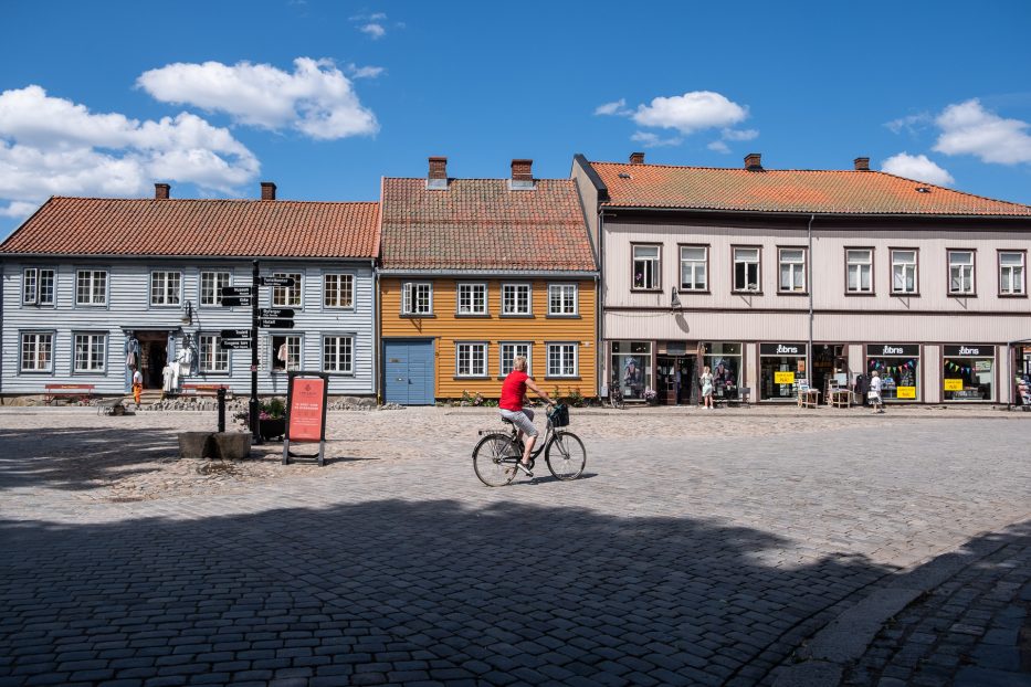 kvinne i rødt på sykkel foran gamle fargerike hus i gamlebyen i Fredrikstad
