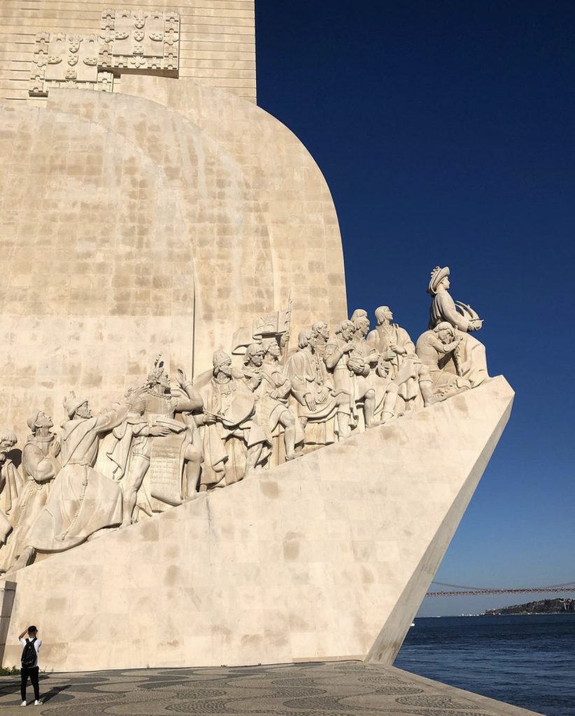 en mann står foran padrao dos Descobrimentos og tar et bilde