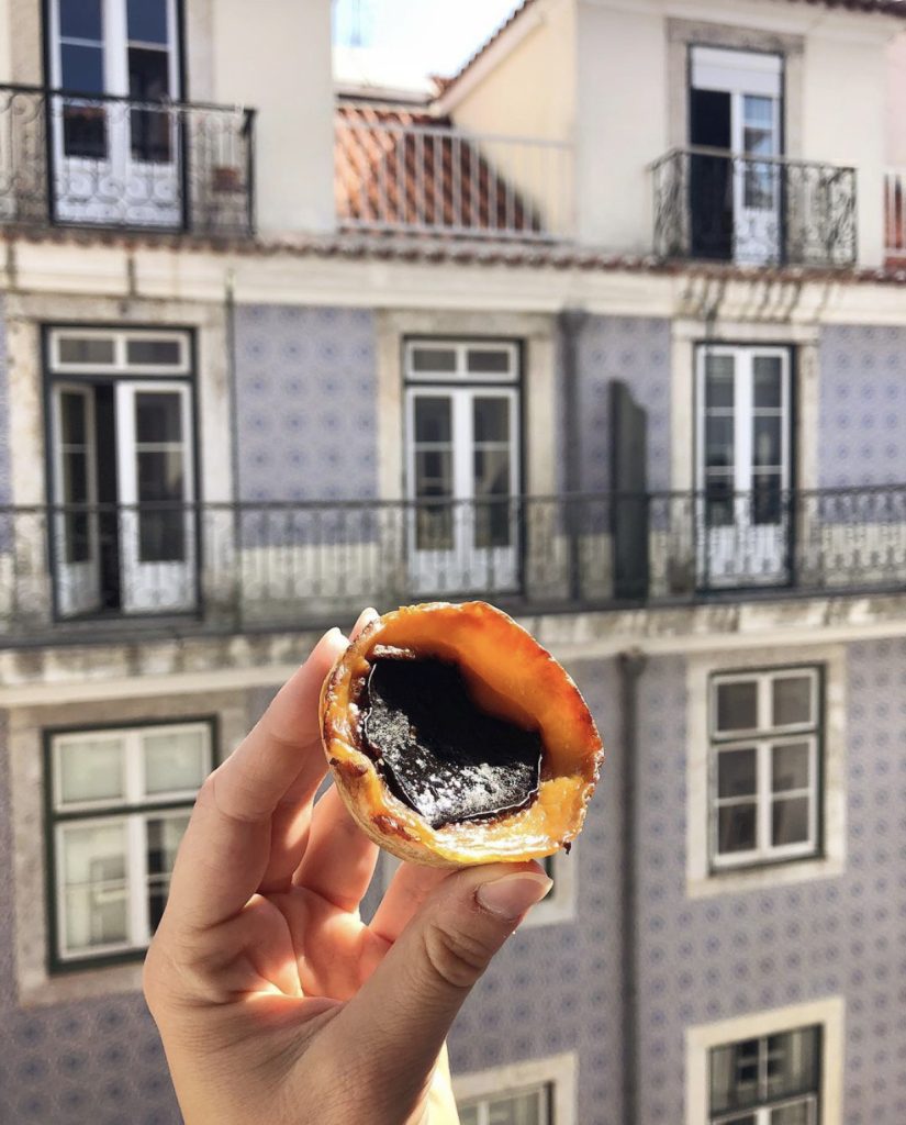 person holding a pastel de nata and Portuguese tiles in the background