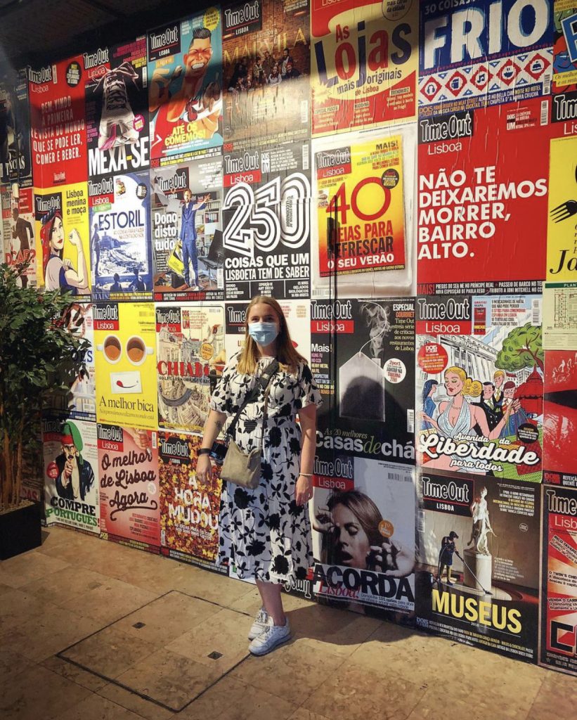 woman wearing a mask in front of a wall filled with colourful posters