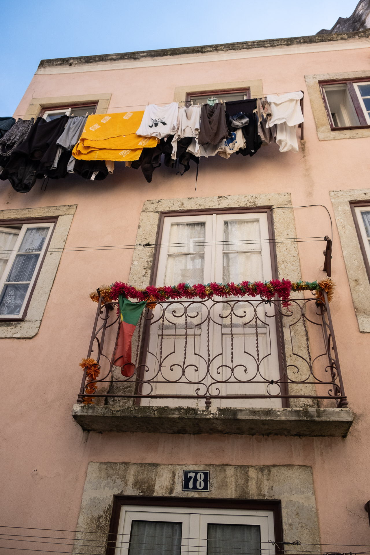 klesvask henger på ei snor langs husfasaden på en bygning med fransk balkong med blomster på