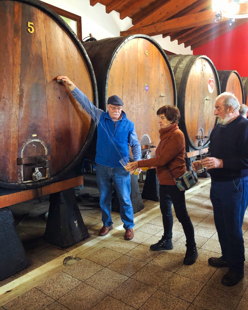 a man pouring cider from a barrel to a woman while a man waits in line