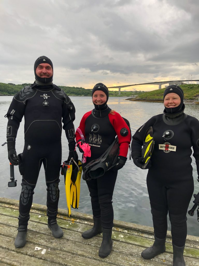 tre personer står på land i tørrdrakter foran saltstraumen