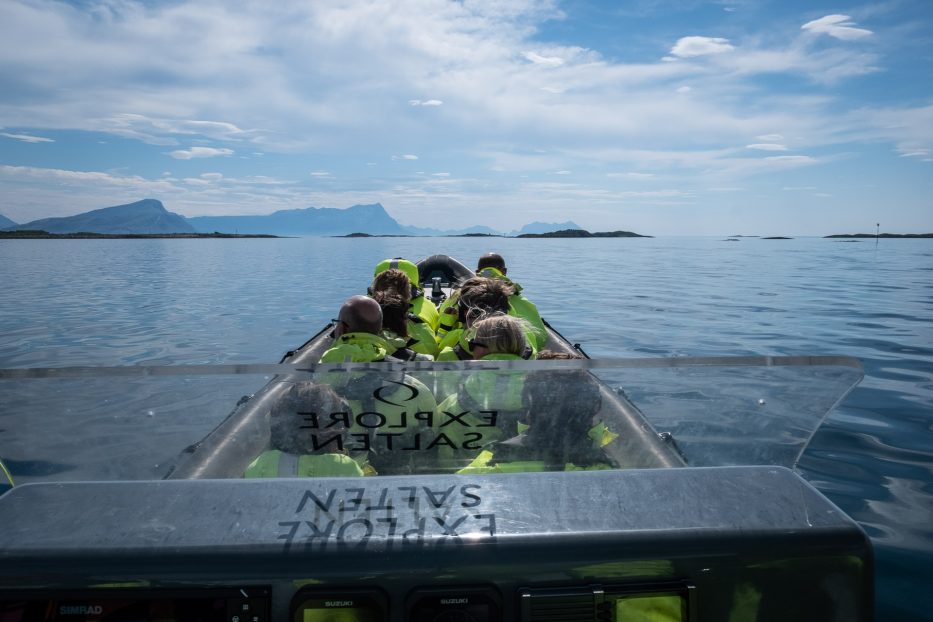 mennesker i en rib-båt på vei utover fra Bodø med fjell i det fjerne
