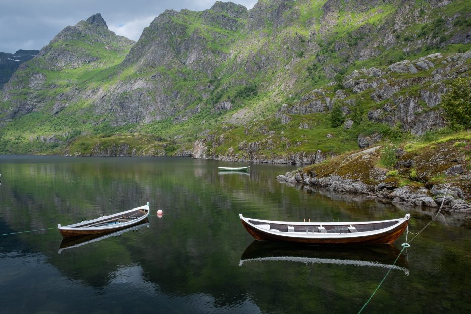 three boats on a calm lake with reflections in water and green mountains in the back