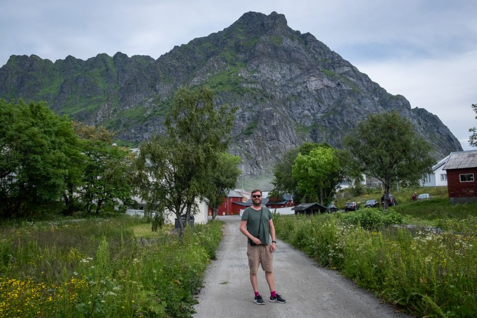 a man in a t-shirt and shorts standing in front of a mountain in lofoten