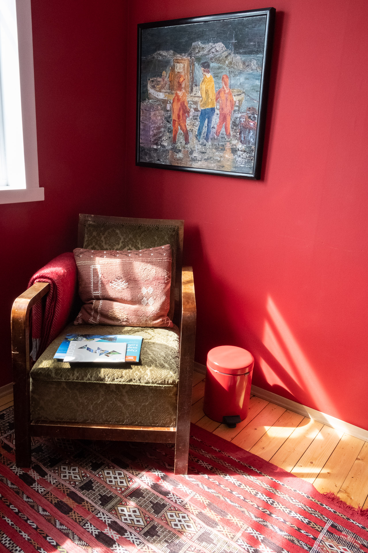 et rødt rom med et fargerikt maleri på veggen og en god stol