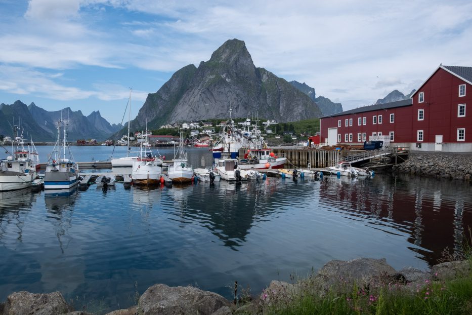 boats and a red house in front of tall mountain in lofoten
