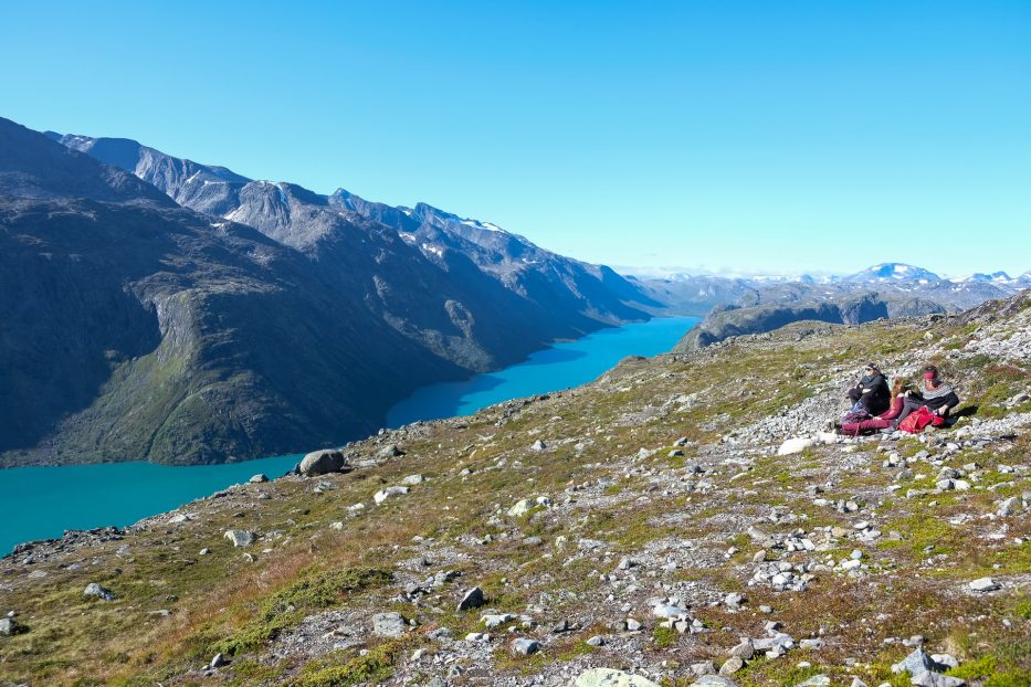 tre personer slapper av med utsikt utover fjorden fra besseggen