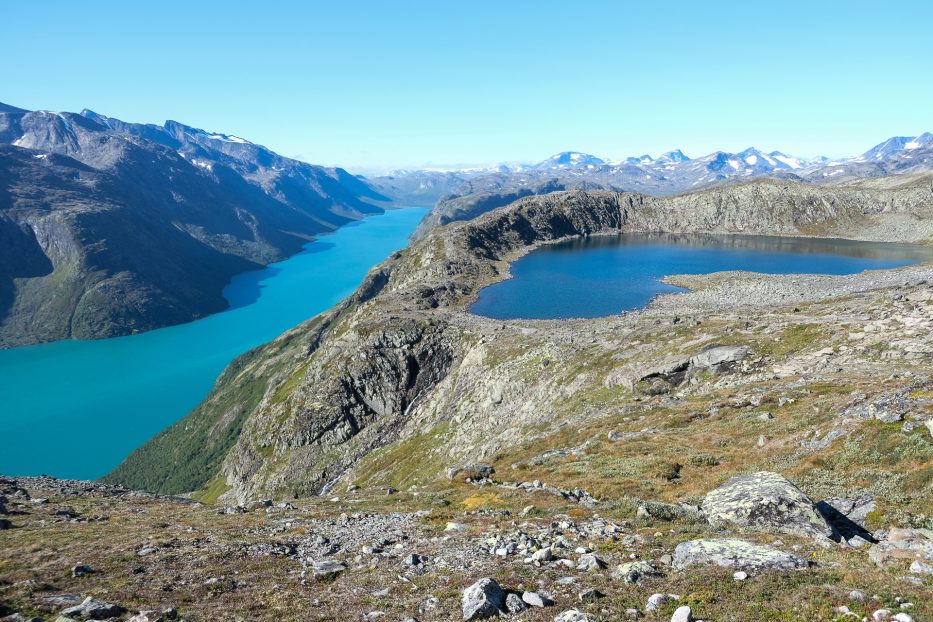 a small lake on top of a hill and a crisp blue lake at the foot of the hill in one picture at besseggen in norway