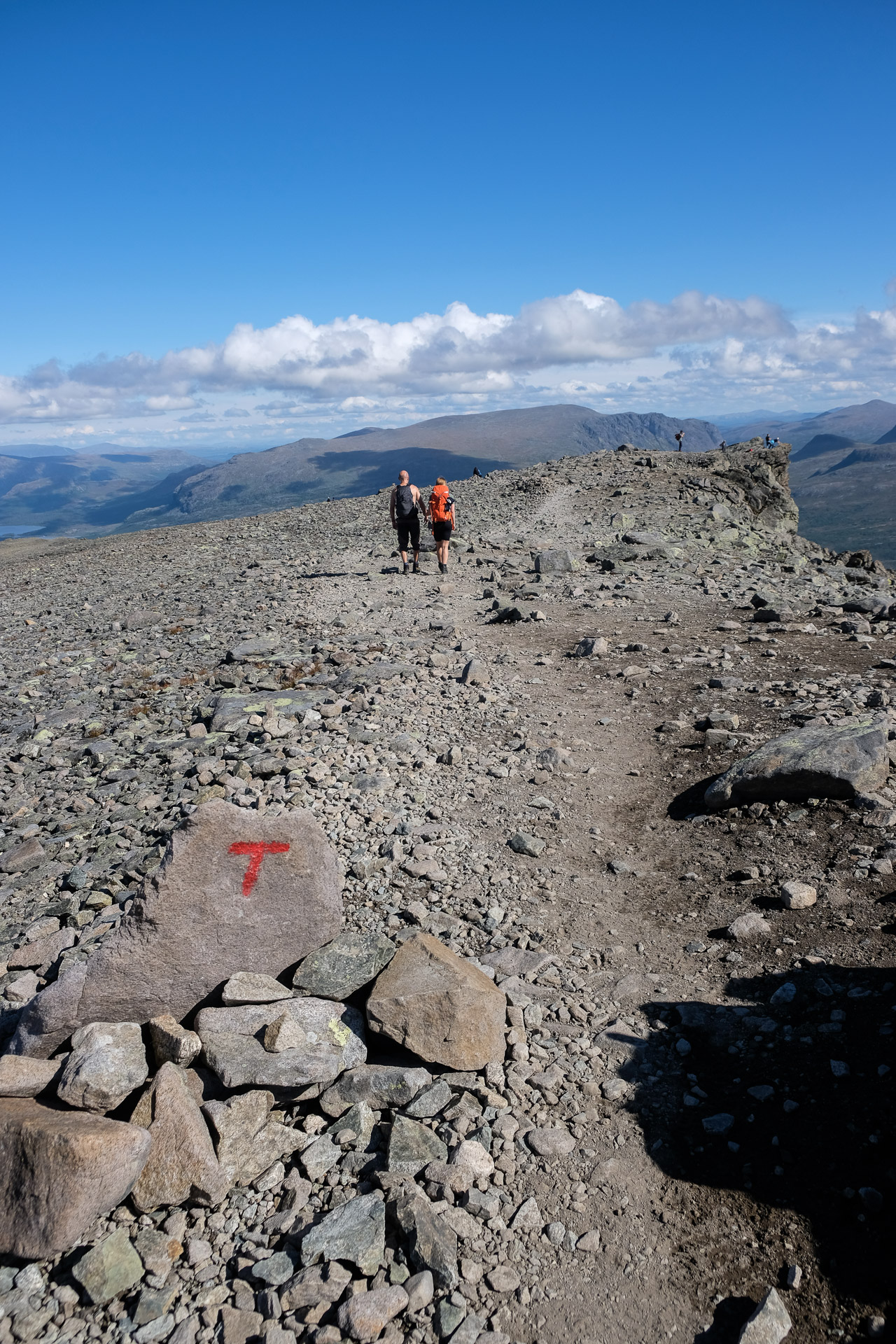 man and woman walking on a gravel road and a rock with a red letter t on it