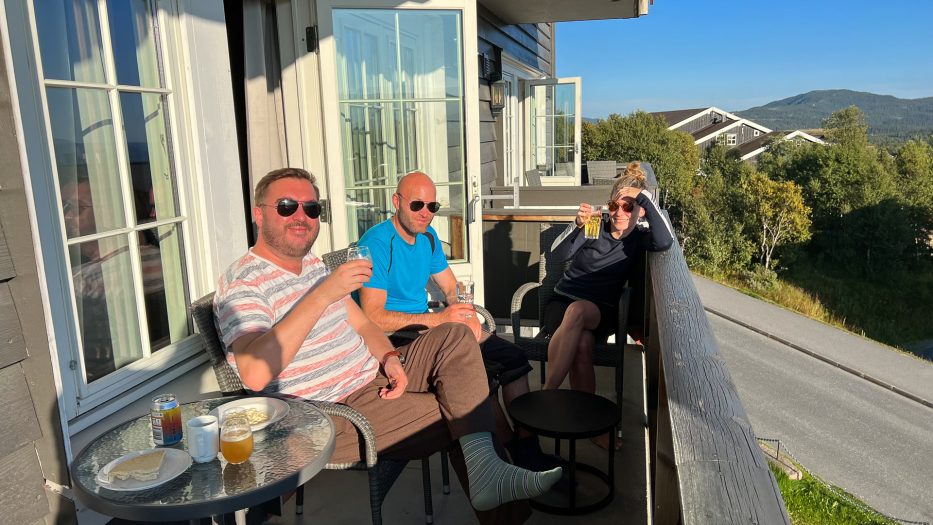two men and a woman with sunglasses enjoying drinks outside in the sun at beitostølenj