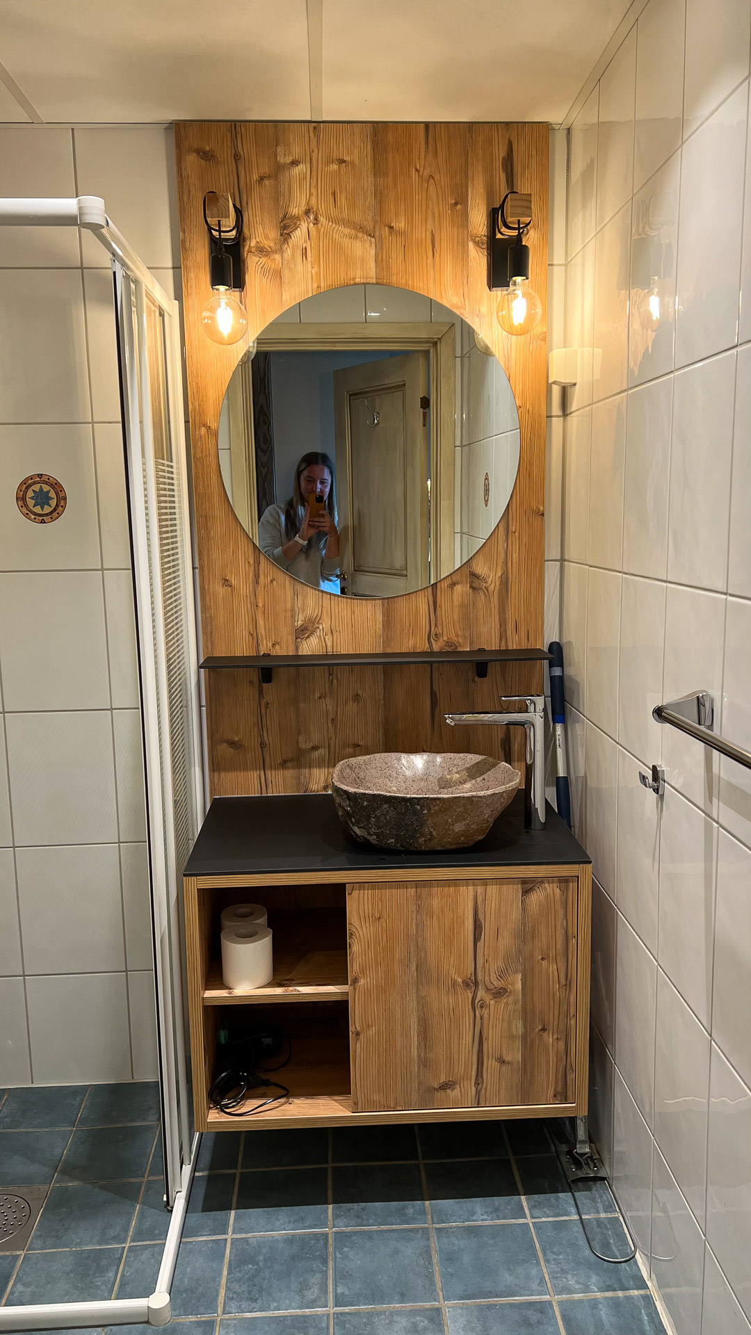 a bathroom with wooden details and a woman reflected in the mirror
