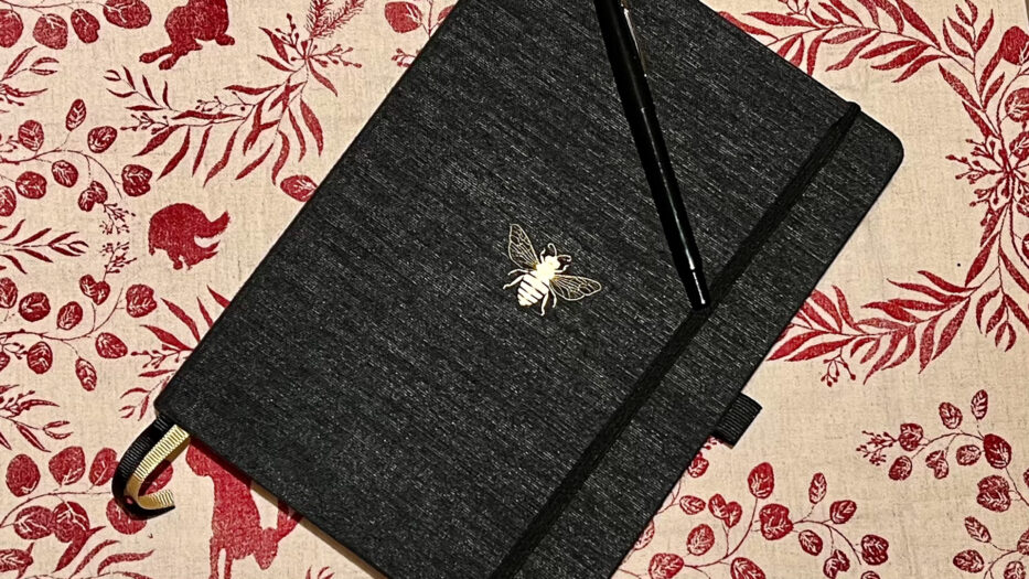 en skrivebok med en bie og en penn oppå liggende på en dekorativ duk