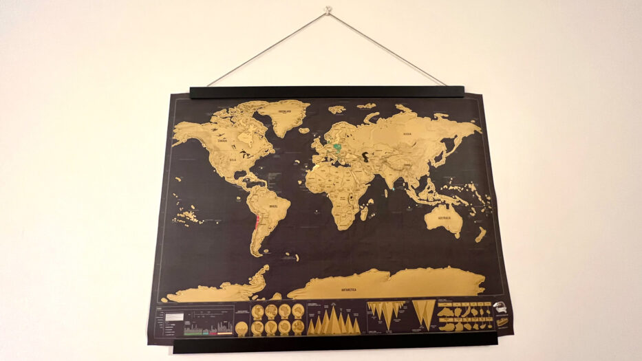 a scratch map of the world in black, with the world in gold, hanging on a wall