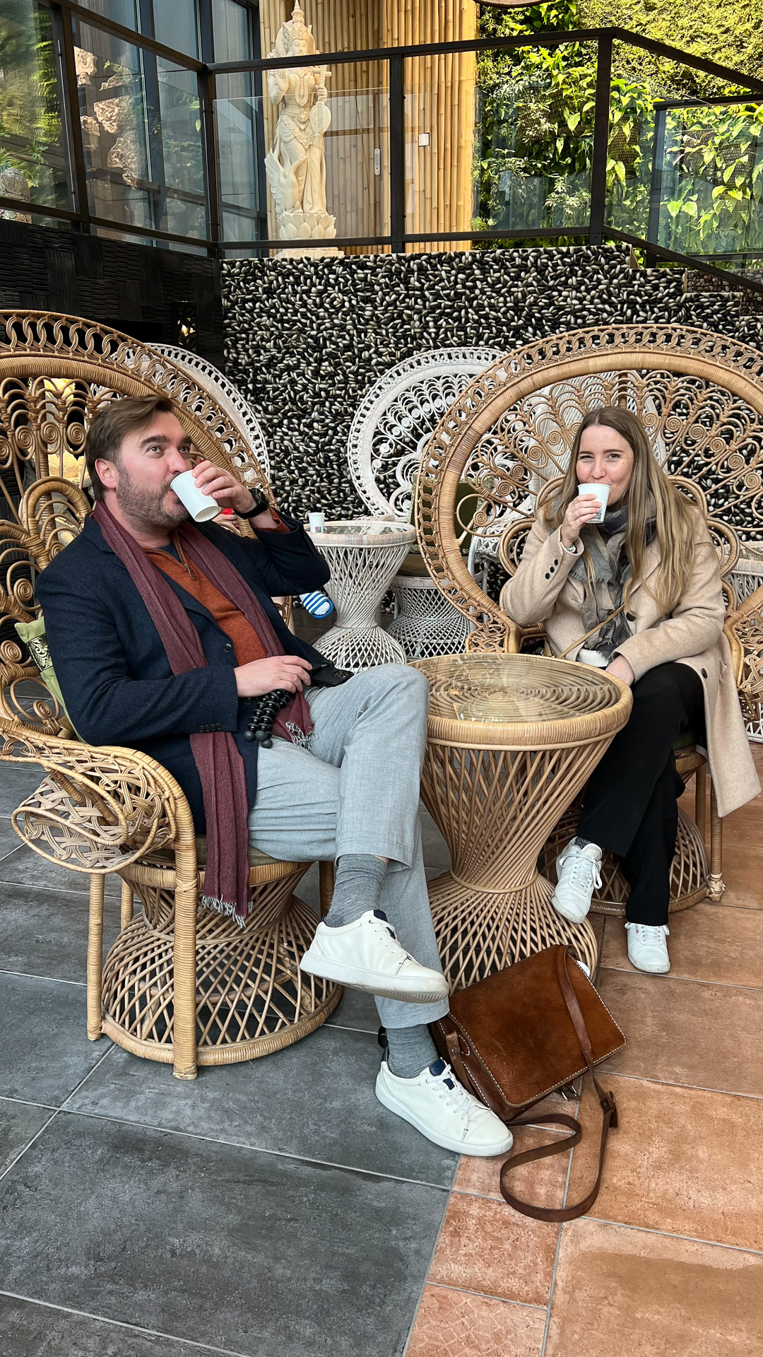 man and woman sitting in fancy bali-inspired chairs in spa drinking mineral water