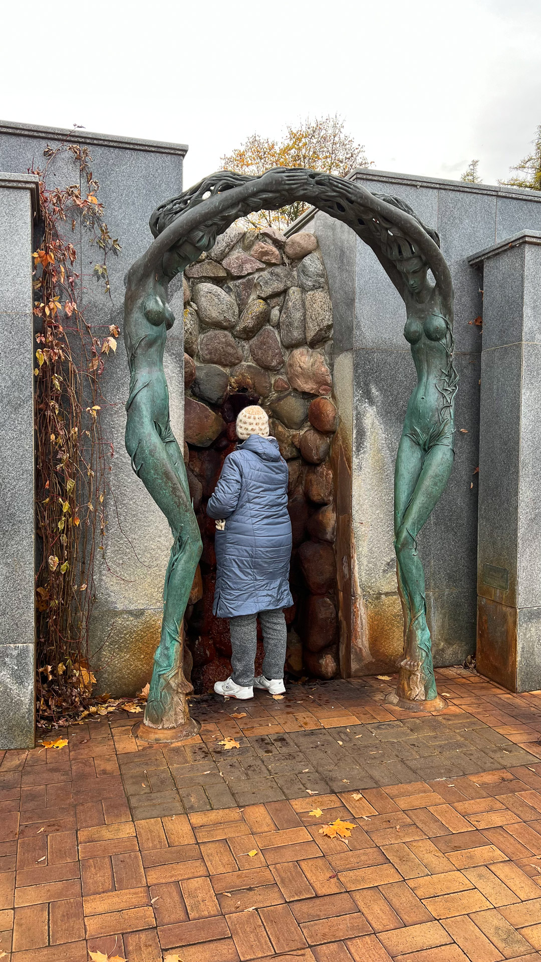 woman in front of mineral water underneath a statue of two women holding hands