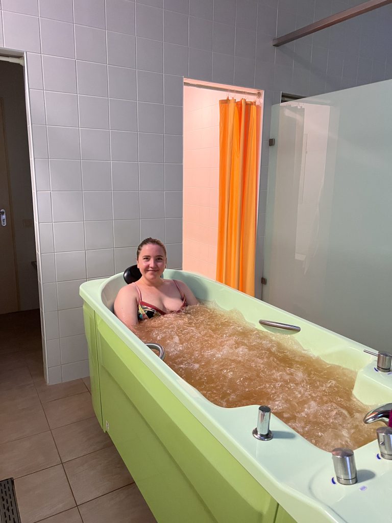 kvinne i bikini sitter i grønt badekar og har et mineralbad hos eglés sanatorija