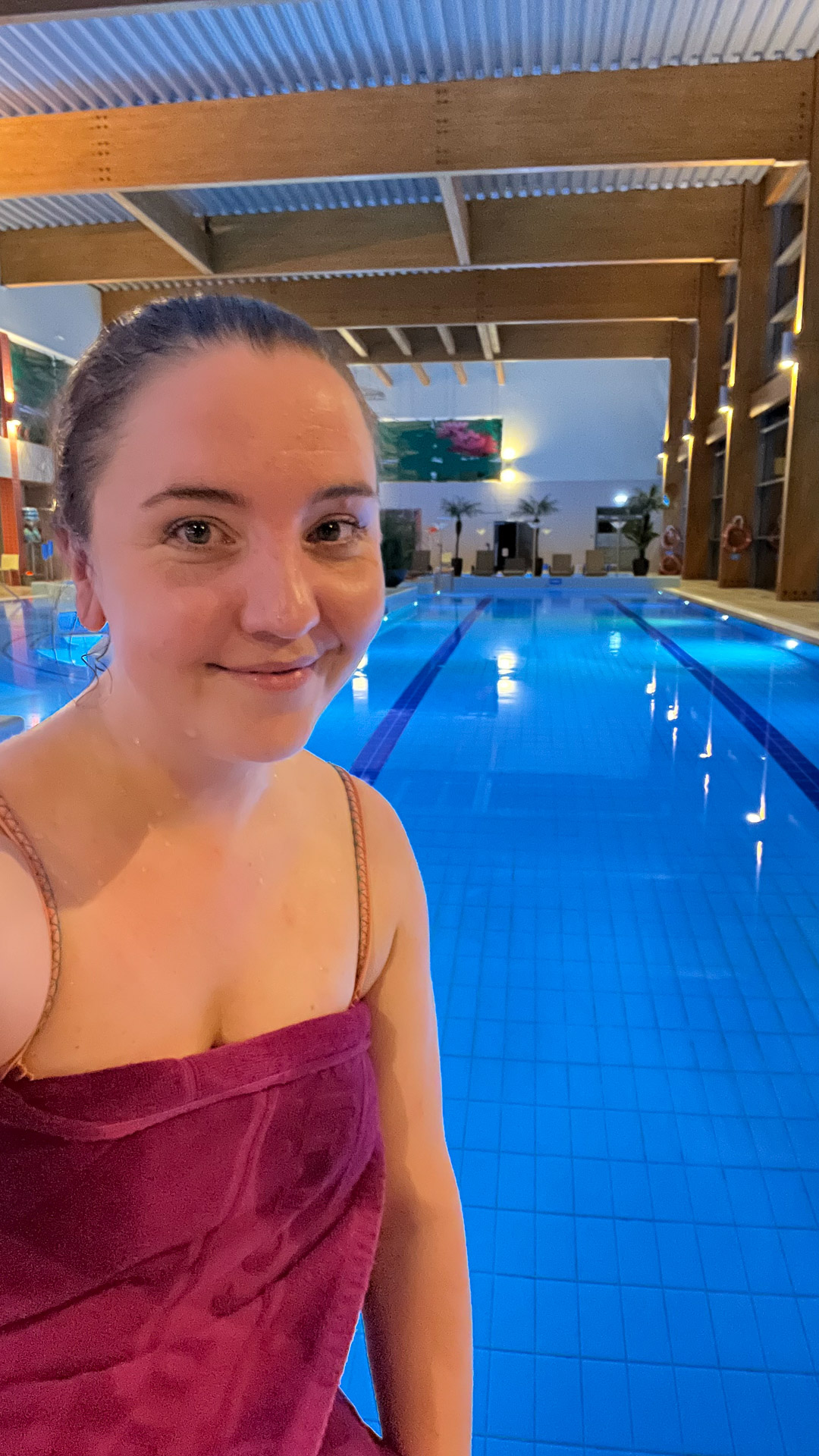 woman with purple towel wrapped around her smiling in front of swimming pool