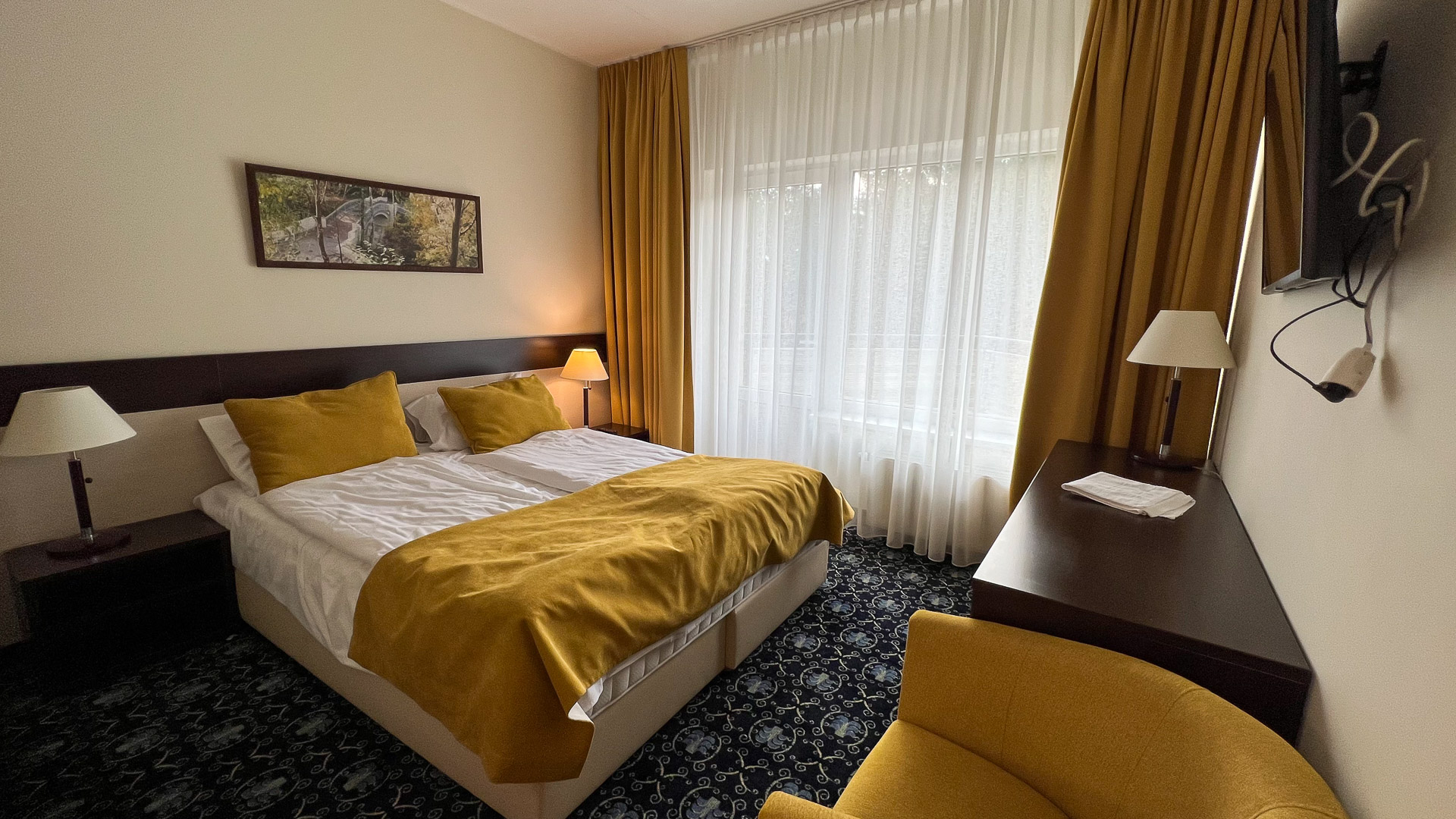 a hotel room with double bed with yellow bedding and curtains