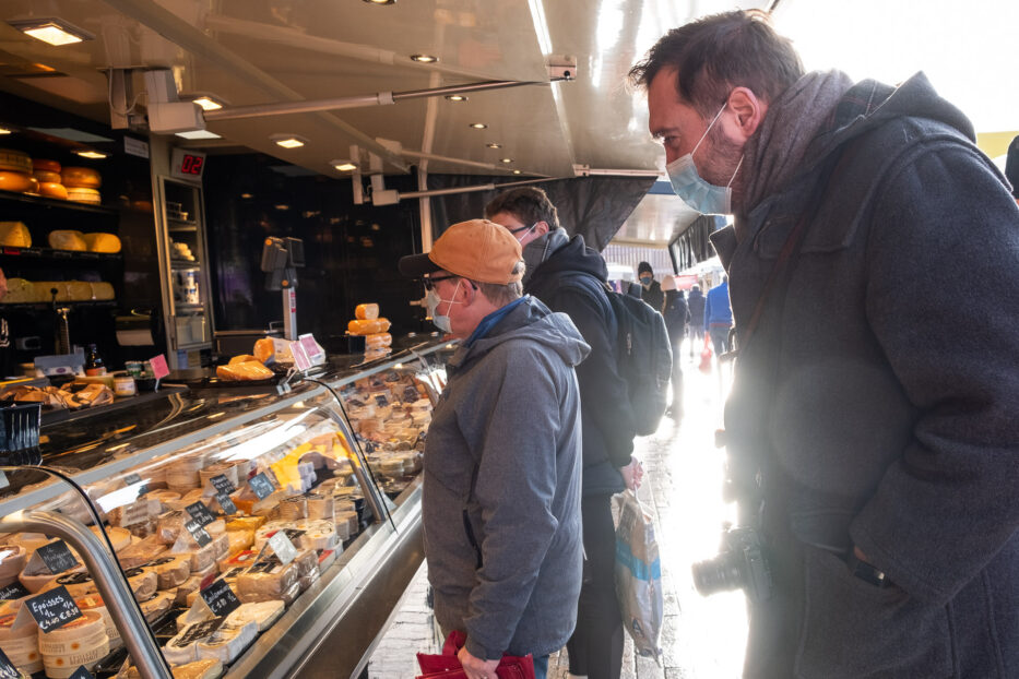 people watching a display of different cheeses at the christmas market in bruges