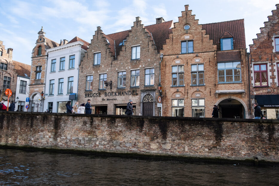 gorgeous stone houses with a bookstore and people walking and the canal of bruges in front