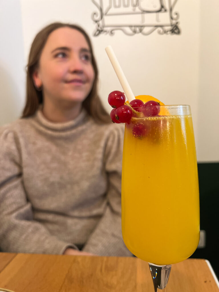 a glass of mimosa and a woman smiling in the background