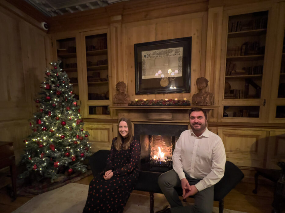 man and woman smiling in front of fireplace and christmas tree at the pand hotel in bruges belgium