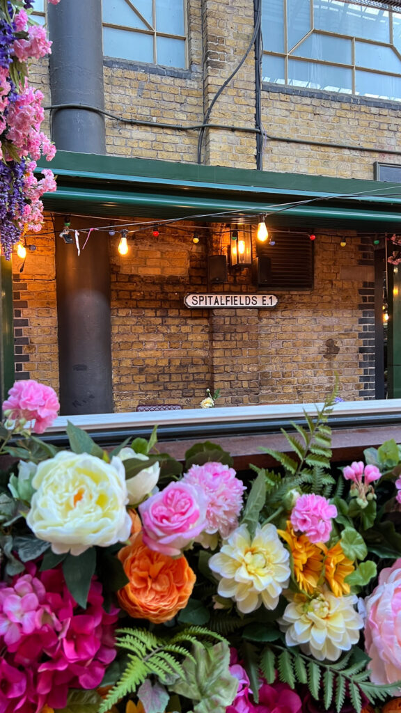 blomster og et skilt på en murvegg med teksten spitalfields market