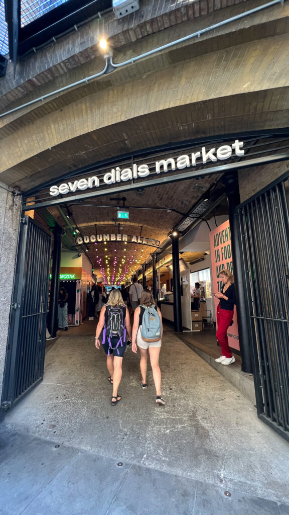 two women walking inside the entrance of sevn dials market in london