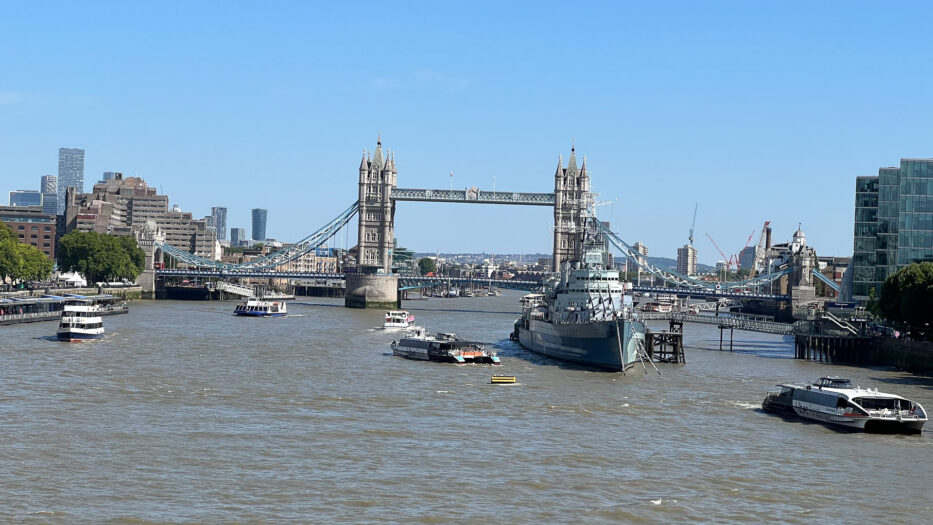 tower bridge i london med en rekke båter og et militærskip i forgrunn