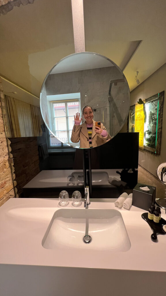 smilende kvinne vinker og tar selfie i et speil på et hotellrom på hotel artagonist i vilnius